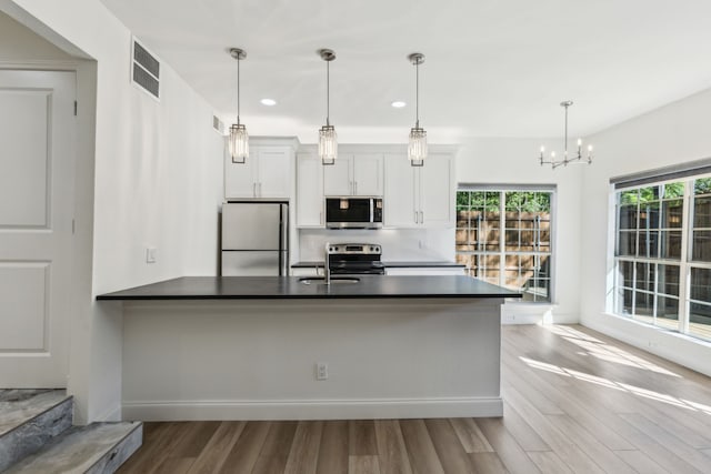 7525 Holly Hill Dr Unit 17, Dallas, TX 75231 - kitchen featuring appliances with stainless steel finishes, dark countertops, wood finished floors, a peninsula, and recessed lighting