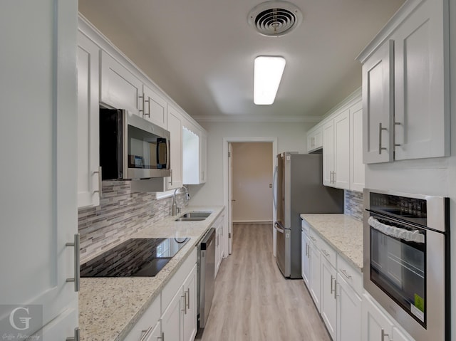 kitchen with stainless steel appliances, a sink, tasteful backsplash, crown molding, and light wood finished floors