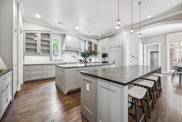 kitchen with custom exhaust hood, a center island, dark countertops, built in appliances, and ornamental molding