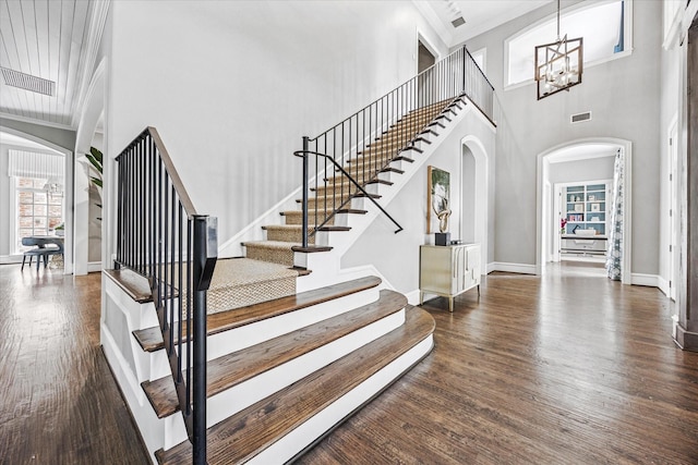 stairway featuring arched walkways, wood finished floors, a towering ceiling, a chandelier, and baseboards