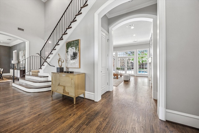 entryway with arched walkways, wood finished floors, ornamental molding, baseboards, and stairs