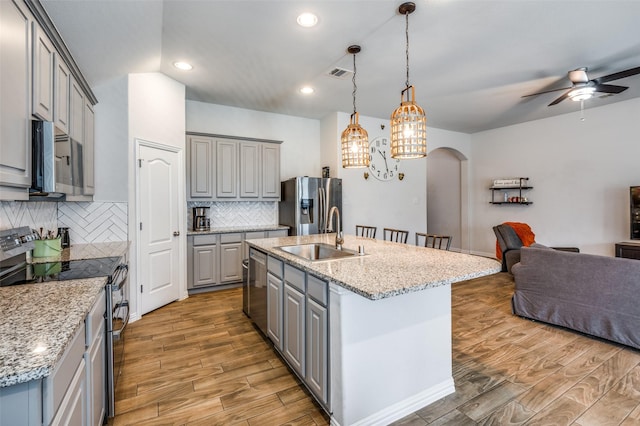 5712 Demi Sec Dr, Mckinney, TX 75070 - kitchen with gray cabinetry, stainless steel appliances, a sink, open floor plan, and light wood finished floors