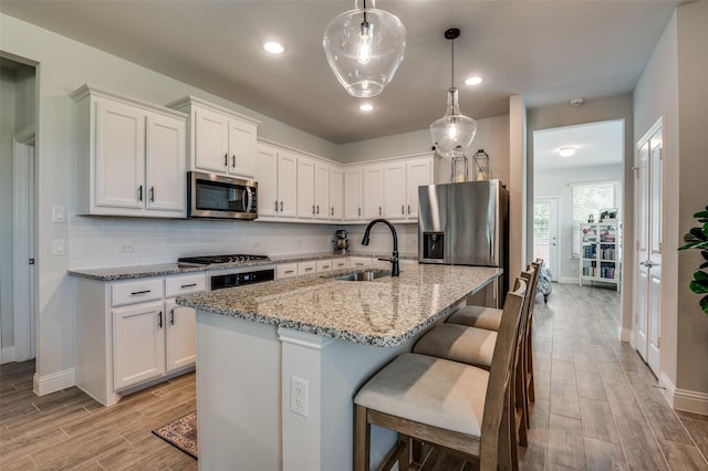kitchen featuring stainless steel appliances, a sink, light wood finished floors, light stone countertops, and baseboards