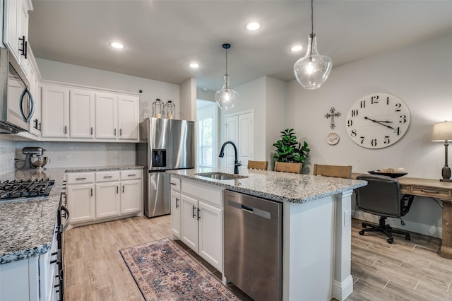 kitchen featuring appliances with stainless steel finishes, a sink, light wood-style flooring, tasteful backsplash, and light stone counters
