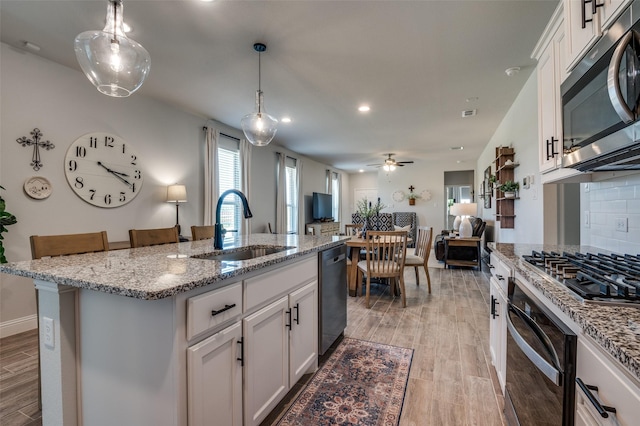 kitchen featuring a sink, black appliances, light wood-style floors, light stone counters, and white cabinets