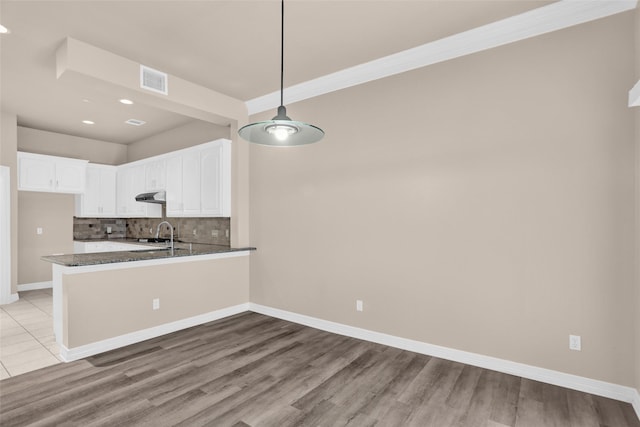 kitchen with tasteful backsplash, white cabinets, dark stone countertops, a peninsula, and a sink