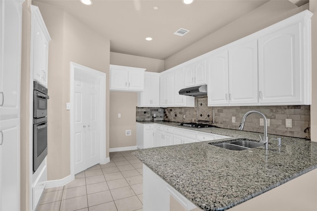 kitchen with a sink, a peninsula, light stone counters, under cabinet range hood, and stainless steel gas stovetop