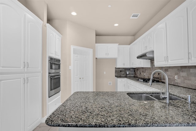 kitchen with a sink, dark stone counters, a peninsula, under cabinet range hood, and recessed lighting