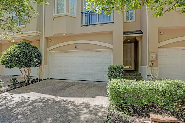 view of front of home with an attached garage, stucco siding, a balcony, and driveway