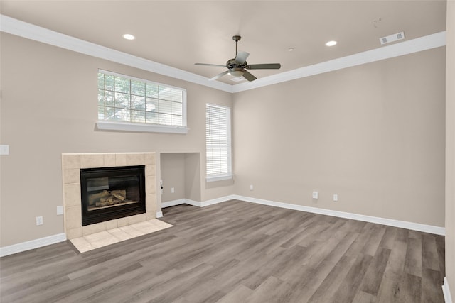 unfurnished living room with ornamental molding, wood finished floors, a tile fireplace, ceiling fan, and baseboards