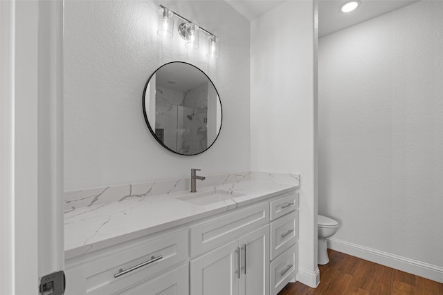 full bath featuring toilet, vanity, wood finished floors, baseboards, and a shower