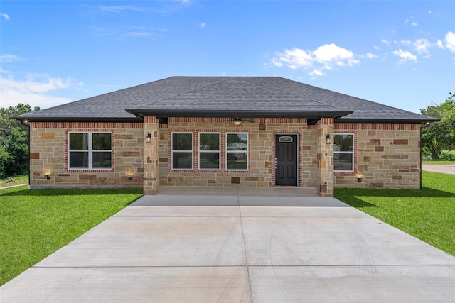 view of front of home with roof with shingles, stone siding, and a front lawn