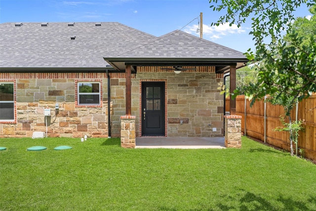 rear view of property featuring a shingled roof, stone siding, a patio, and a ceiling fan