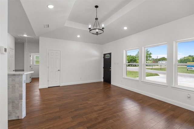 unfurnished living room with a tray ceiling, healthy amount of natural light, dark wood-type flooring, a chandelier, and recessed lighting