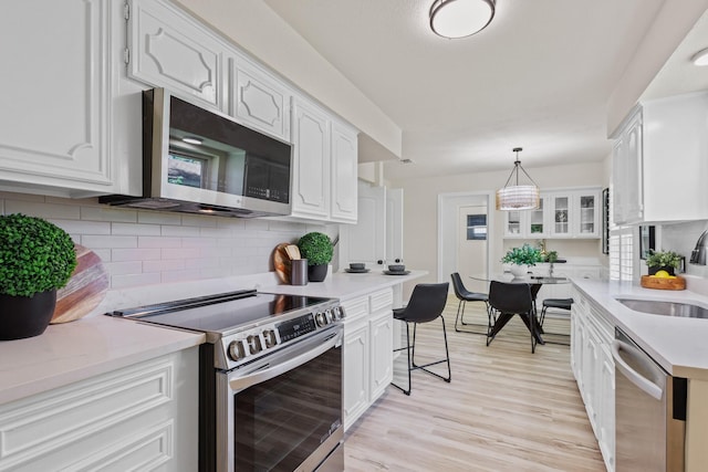 2809 Valley Ridge Dr, Richardson, TX 75080 - kitchen with stainless steel appliances, white cabinets, light countertops, a sink, and light wood-style flooring