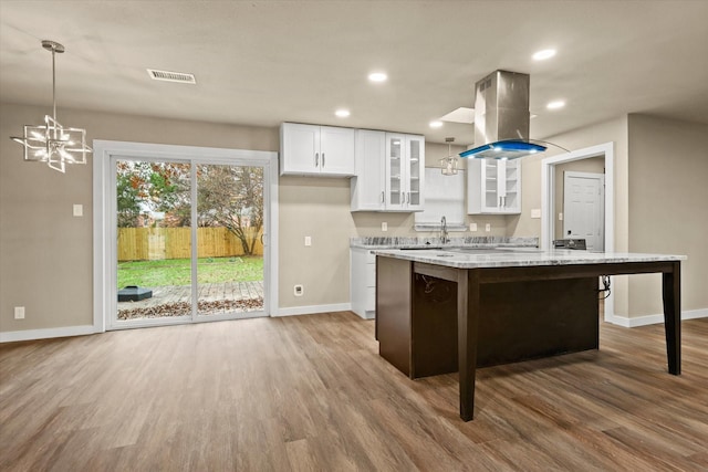 612 S Mills Dr, Euless, TX 76040 - kitchen with island range hood, white cabinetry, wood finished floors, baseboards, and a chandelier