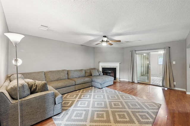 4841 Woodstock Dr, Fort Worth, TX 76137 - living area with a ceiling fan, wood finished floors, a tiled fireplace, a textured ceiling, and baseboards