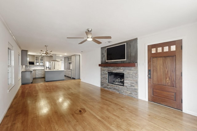 6723 Blessing Dr, Dallas, TX 75214 - unfurnished living room with a ceiling fan, a stone fireplace, light wood-type flooring, ornamental molding, and baseboards