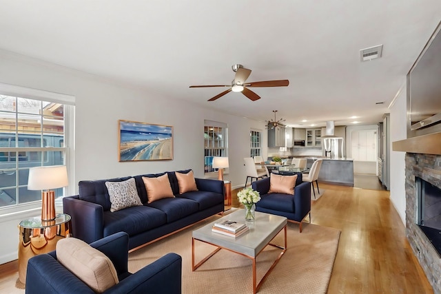 6723 Blessing Dr, Dallas, TX 75214 - living area featuring ceiling fan, light wood finished floors, a stone fireplace, and a chandelier