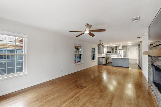 6723 Blessing Dr, Dallas, TX 75214 - unfurnished living room with a stone fireplace, light wood-style flooring, a ceiling fan, a chandelier, and baseboards