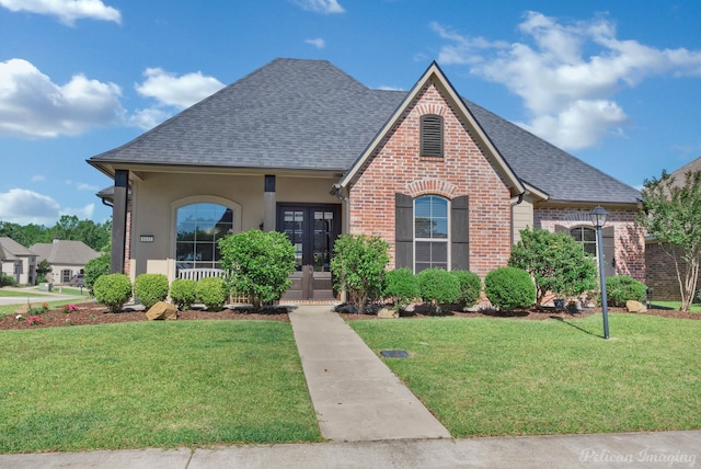 view of front facade featuring roof with shingles, brick siding, a front yard, and french doors