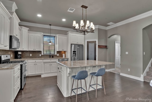 kitchen featuring appliances with stainless steel finishes, a sink, arched walkways, ornamental molding, and a center island