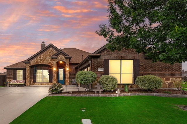 french country inspired facade featuring brick siding, a front yard, a chimney, and stone siding