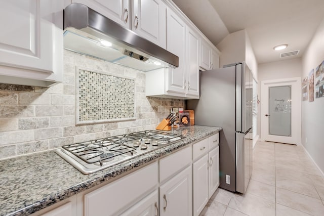 kitchen featuring under cabinet range hood, white cabinets, freestanding refrigerator, gas stovetop, and tasteful backsplash