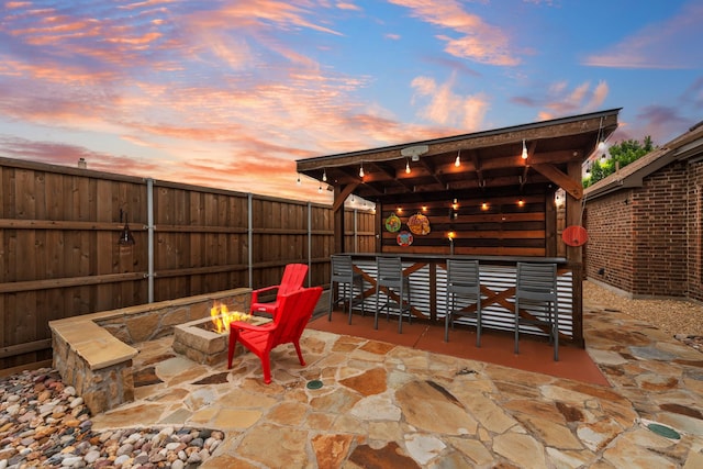 patio terrace at dusk featuring an outdoor fire pit and a fenced backyard