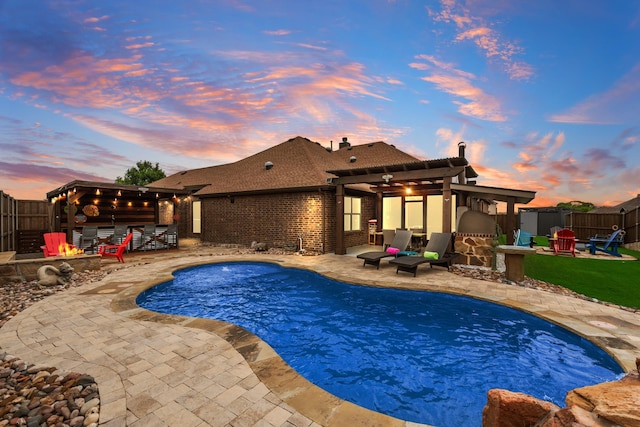 pool at dusk with a fire pit, a patio area, and a fenced backyard