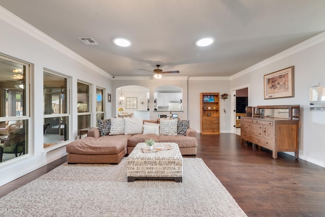 living area with ornamental molding, a ceiling fan, arched walkways, dark wood-type flooring, and baseboards