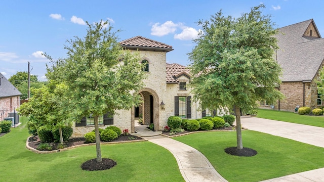 mediterranean / spanish home featuring a tiled roof, a front lawn, and stone siding