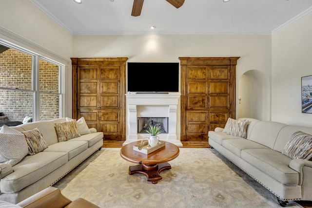 living room featuring ceiling fan, wood finished floors, arched walkways, ornamental molding, and a fireplace with raised hearth