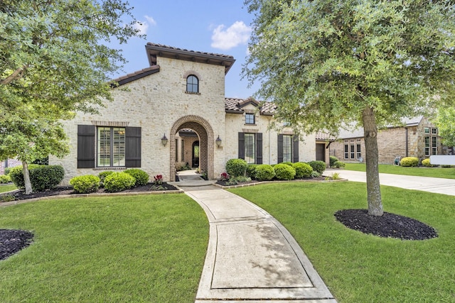 mediterranean / spanish home with a tile roof, a front lawn, stucco siding, and stone siding