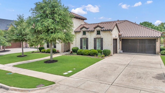 mediterranean / spanish home featuring driveway, a garage, a tiled roof, a front yard, and stone siding