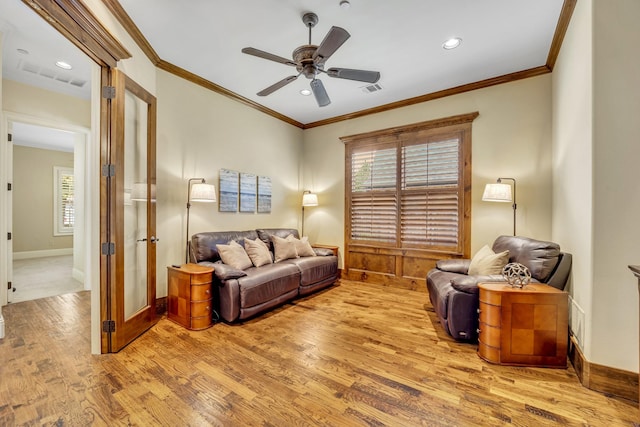 living area with wood finished floors, ornamental molding, plenty of natural light, a ceiling fan, and baseboards