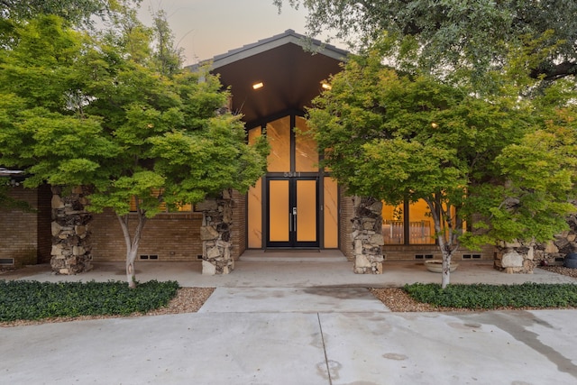 5511 Royal Ln, Dallas, TX 75229 - exterior entry at dusk featuring french doors, brick siding, crawl space, and stone siding