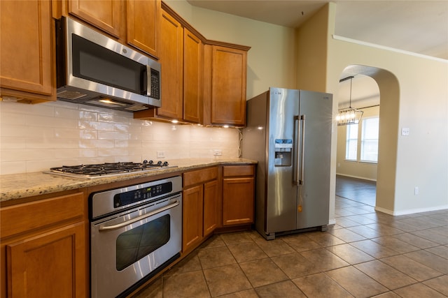 4356 Mountain Crest Dr, Fort Worth, TX 76123 - kitchen with stainless steel appliances, tasteful backsplash, arched walkways, dark tile patterned flooring, and brown cabinets