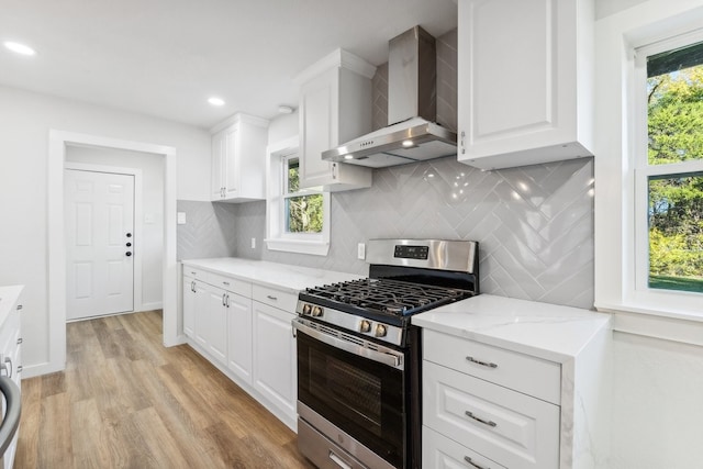 kitchen featuring stainless steel range with gas stovetop, wall chimney exhaust hood, light wood-style flooring, white cabinets, and recessed lighting