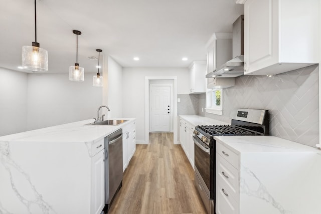 kitchen featuring appliances with stainless steel finishes, a sink, wall chimney range hood, light wood finished floors, and tasteful backsplash