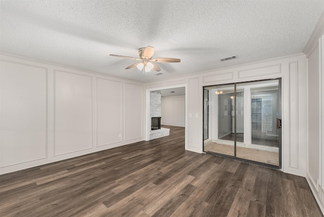 spare room with a decorative wall, ceiling fan, a brick fireplace, dark wood-type flooring, and a textured ceiling