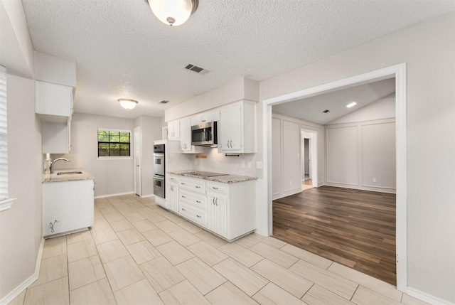 kitchen with a sink, appliances with stainless steel finishes, a textured ceiling, white cabinetry, and light stone counters