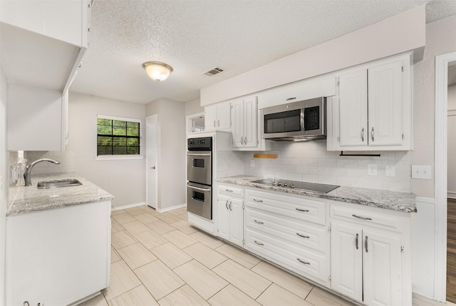kitchen featuring a sink, appliances with stainless steel finishes, a textured ceiling, decorative backsplash, and baseboards