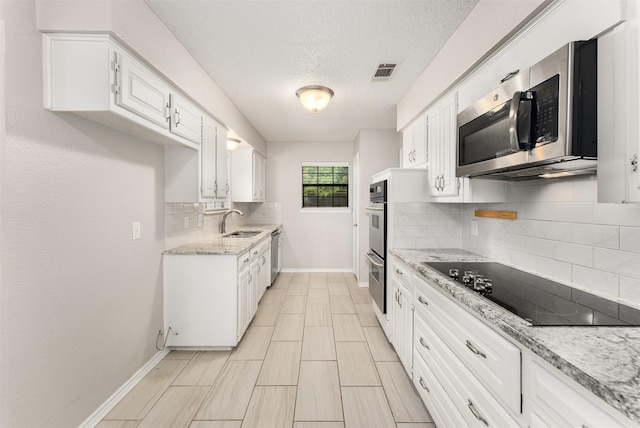kitchen featuring stainless steel appliances, a sink, white cabinets, baseboards, and backsplash