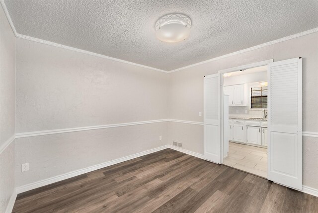 unfurnished room with a textured ceiling, dark wood-style floors, a sink, crown molding, and baseboards