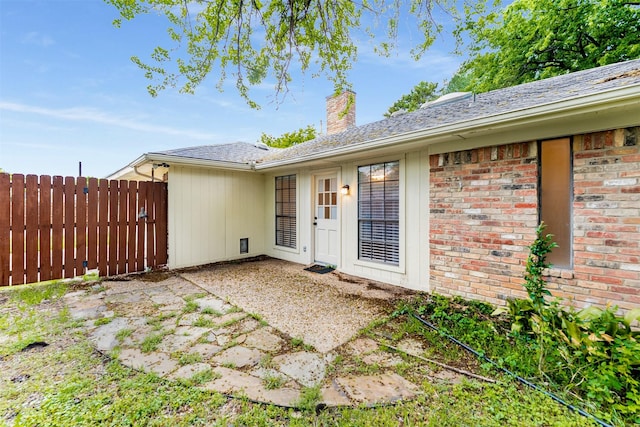 view of exterior entry with fence, a chimney, a patio area, and brick siding
