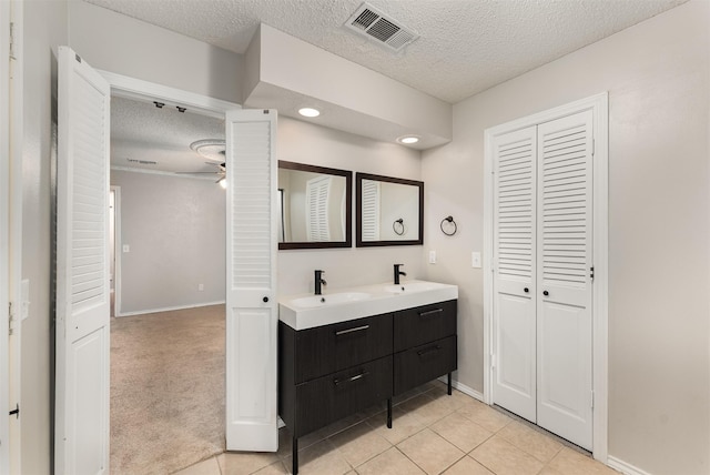 full bathroom with a textured ceiling, baseboards, double vanity, a closet, and tile patterned floors