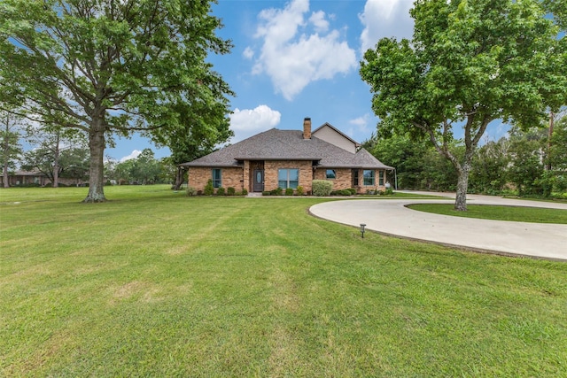 view of front of property with brick siding, curved driveway, a chimney, and a front lawn