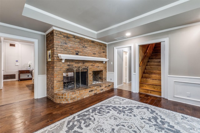 unfurnished living room featuring wood-type flooring, a fireplace, ornamental molding, a wainscoted wall, and stairs