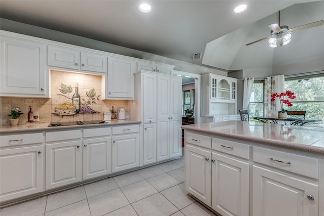 kitchen with light tile patterned floors, black electric cooktop, light countertops, vaulted ceiling, and backsplash
